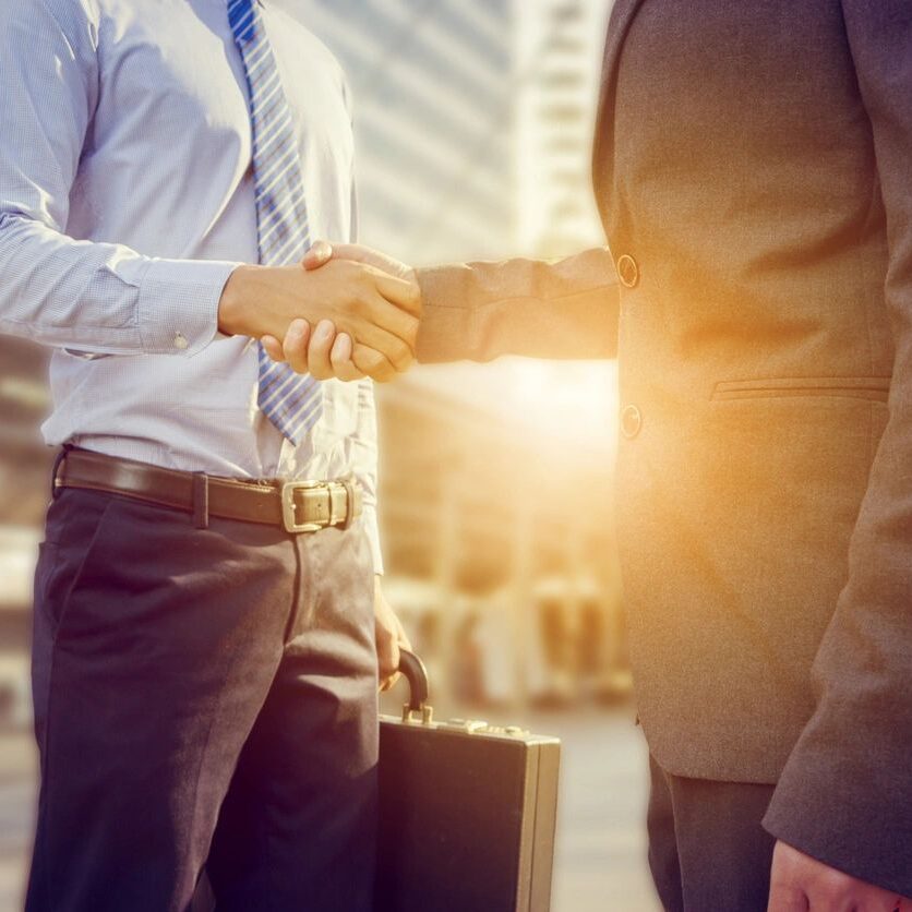 Two men shaking hands in front of a building.